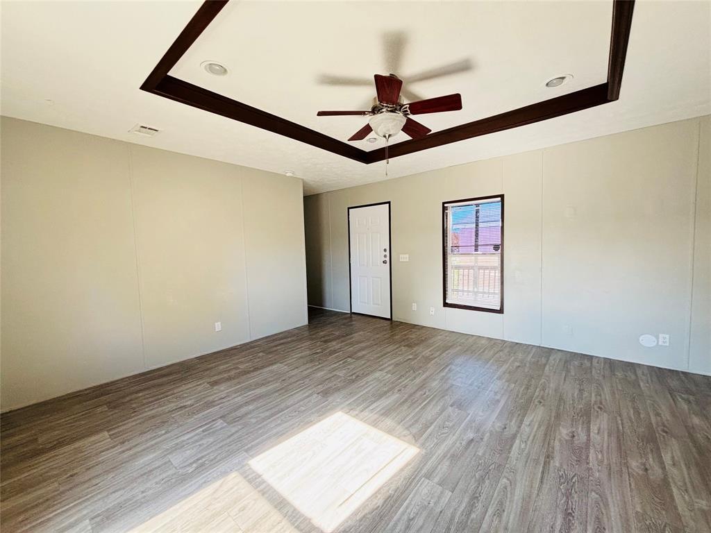 Tray ceiling with dark wood-finish trim, wood-finish flooring, ceiling fan with integrated light fixture, recessed lighting, and single-panel exterior door