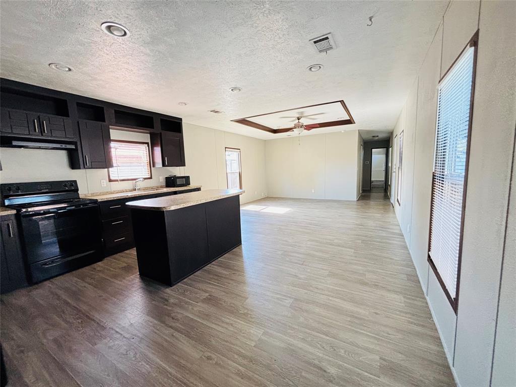 Kitchen featuring dark cabinetry, an island with stone-finish countertop, wood-finish flooring, recessed lighting, and a coffered ceiling with integrated ceiling fan