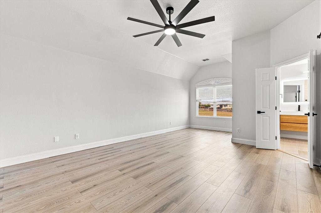 Vaulted ceilings, wood-finish flooring, multi-blade modern ceiling fan, arched window, and paneled doors with matte black hardware