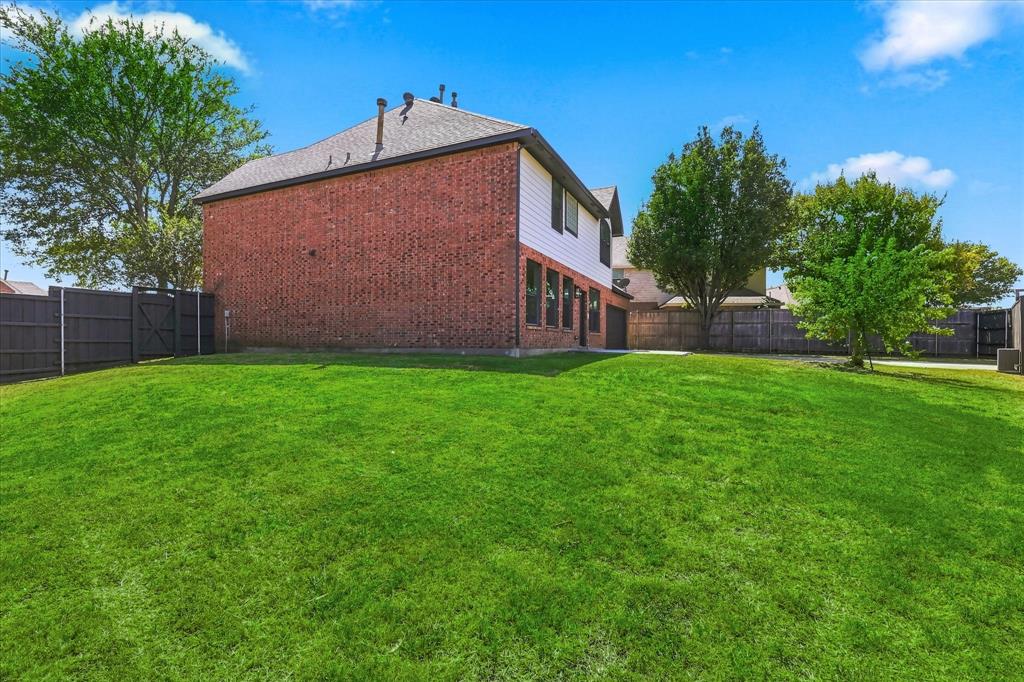 Rear exterior featuring red brick and white horizontal siding, a gabled roof, expansive grass lawn, and full-perimeter wood privacy fencing