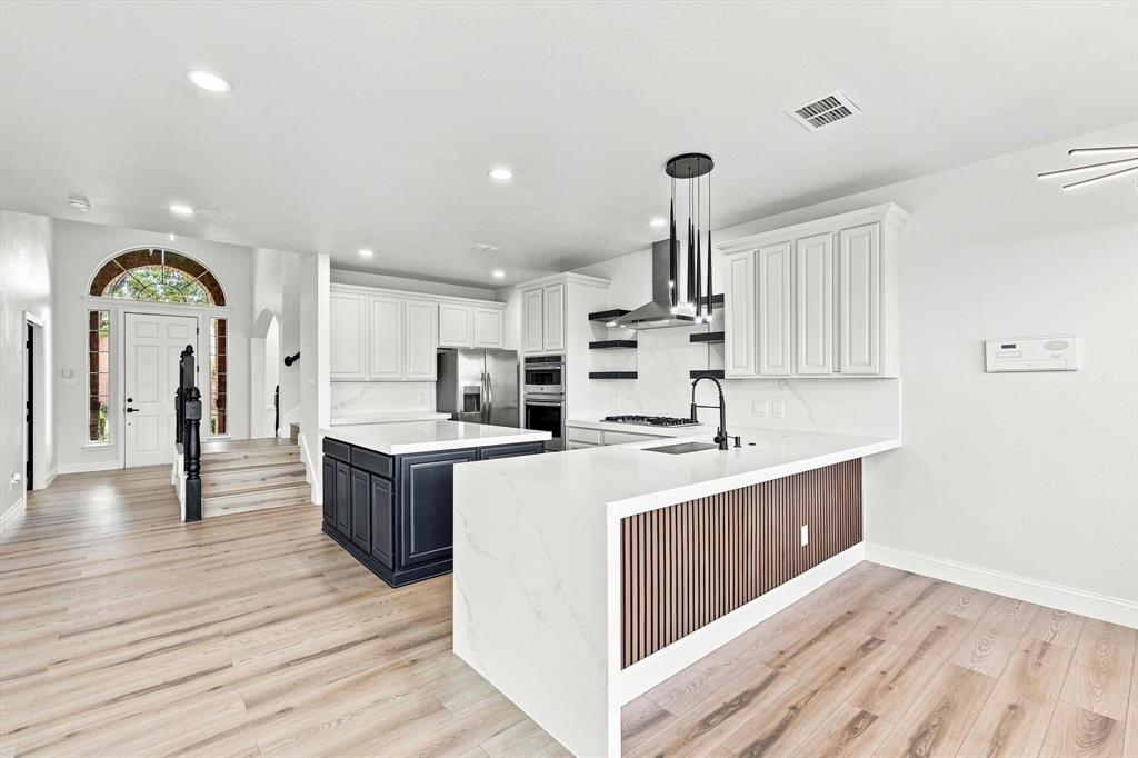 Kitchen featuring quartz countertops, wood-finish flooring, two-tone cabinetry, a fluted wood kitchen island base, and stainless steel built-in appliances