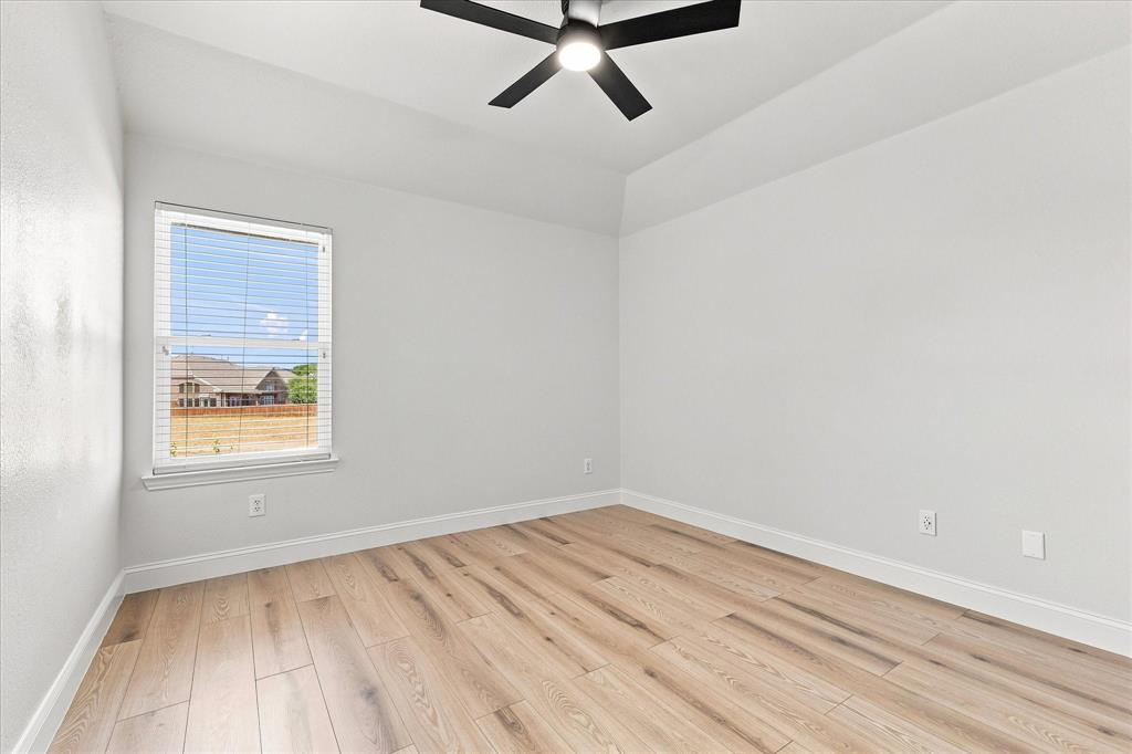 Neutral-toned interior room featuring wood-finish flooring, tray ceiling, and a modern black ceiling fan with integrated lighting
