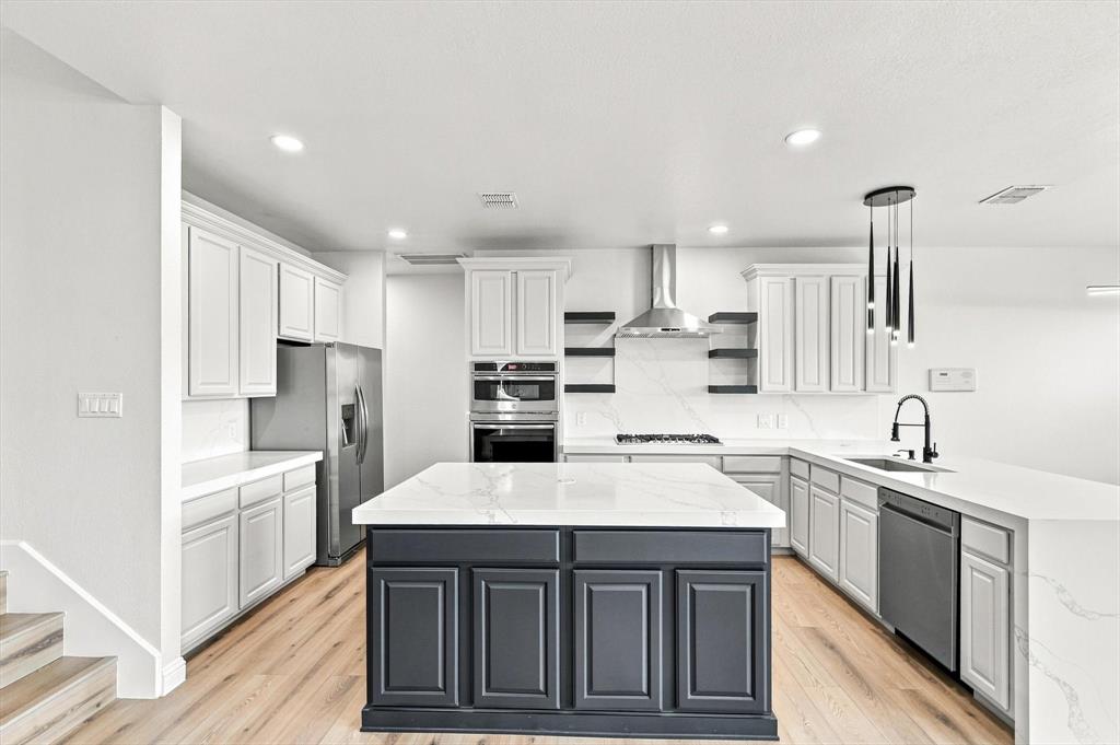 Kitchen featuring white cabinetry, a contrasting dark-toned center island with quartz countertops, stainless steel appliances, stone-look backsplash, and wood-finish flooring
