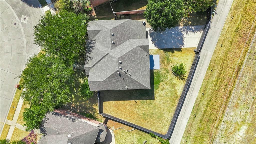 Aerial perspective featuring a multi-faceted shingle roof, concrete driveway, and a fenced backyard with mature trees
