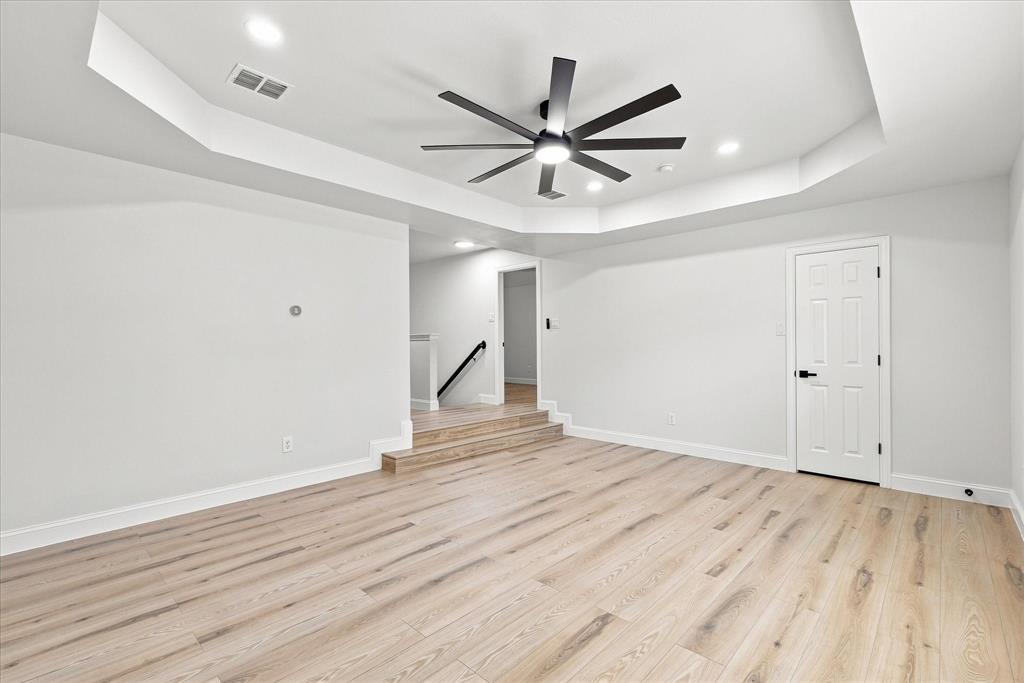 Tray ceiling featuring a multi-blade ceiling fan, recessed lighting, and wood-finish flooring with a step-up elevation change