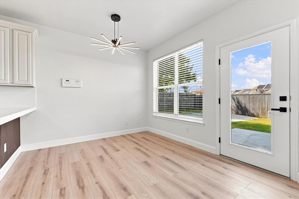 Interior space featuring wood-finish flooring, a modern multi-arm sputnik-style chandelier, horizontal window blinds, and a glass-paneled exterior door with matte black hardware