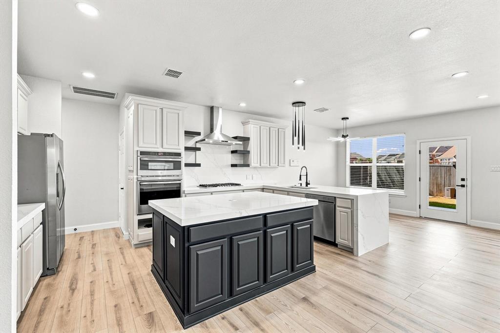 Kitchen featuring wood-finish flooring, a central island with contrasting cabinetry, stone-finish countertops, stainless steel appliances, and built-in wall ovens
