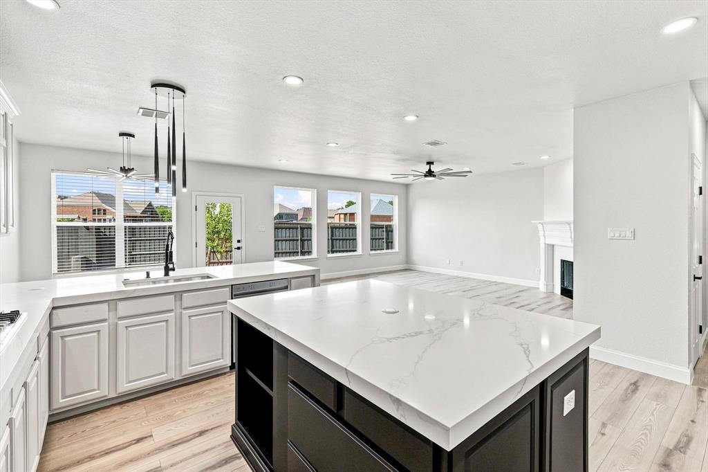 Kitchen featuring a central island with a stone-finish countertop, white cabinetry, wood-finish flooring, recessed lighting, and a fireplace with a decorative mantel