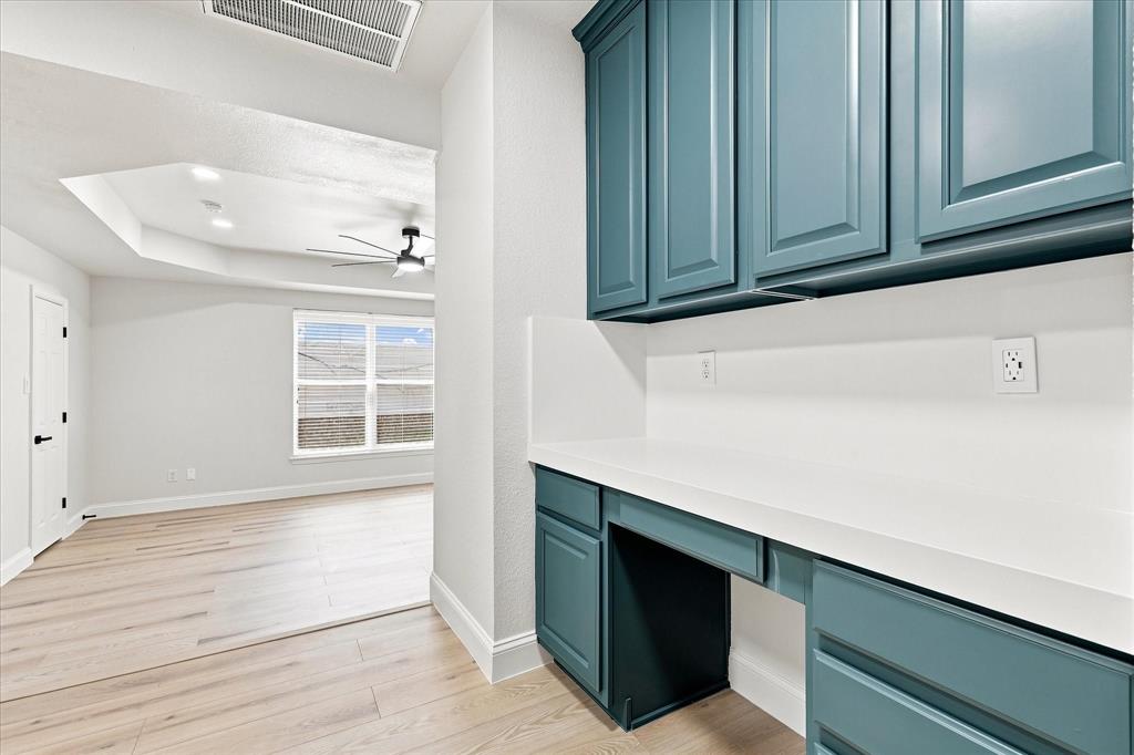 Built-in desk featuring teal cabinetry, white solid-surface countertop, wood-finish flooring, and recessed tray ceiling