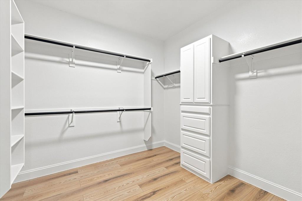 Walk-in closet featuring wood-finish flooring, built-in white cabinetry with drawers, shelving units, and double-tier hanging rods