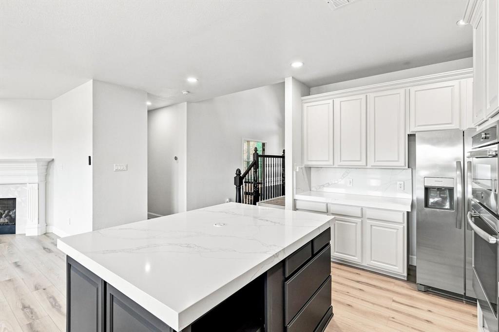 Kitchen featuring white cabinetry, an oversized central island with a contrasting dark finish and stone countertop, stainless steel appliances, and wood-finish flooring
