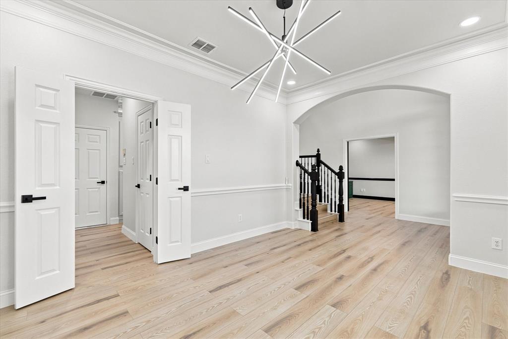 Interior space featuring wood-finish flooring, crown molding, chair rail trim, a multi-arm geometric chandelier, and an arched entry with a staircase
