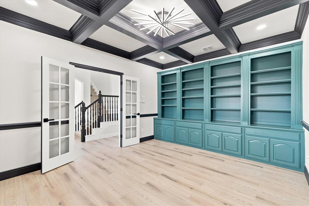 Coffered ceiling with contrasting dark beams, custom built-in teal shelving, wood-finish flooring, glass-paneled French doors, and recessed lighting