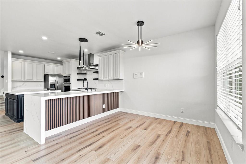 Kitchen featuring wood-finish flooring, a waterfall-edge stone countertop, vertical wood-slat island detailing, white cabinetry, and modern geometric pendant lighting