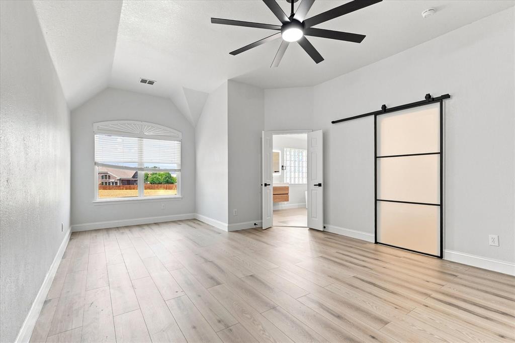 Vaulted ceilings, wood-finish flooring, multi-pane window with arched transom, matte black ceiling fan, and sliding barn door with frosted glass panels