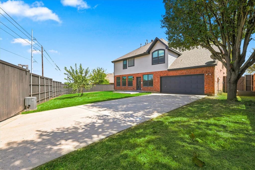 Exterior featuring brick and horizontal siding construction, an attached two-car garage, an expansive concrete driveway, a privacy fence, and mature trees
