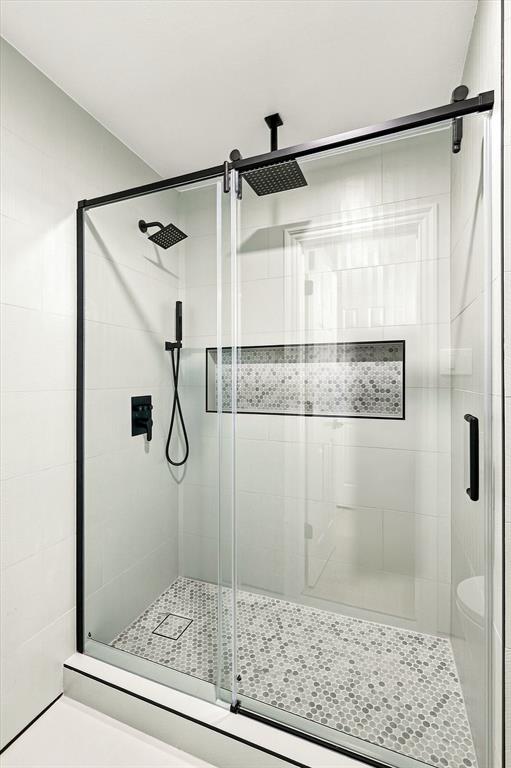 Walk-in shower featuring a frameless glass sliding door with matte black hardware, rainfall showerhead, adjustable handheld shower wand, and a built-in recessed tiled niche with hexagonal mosaic tile accents