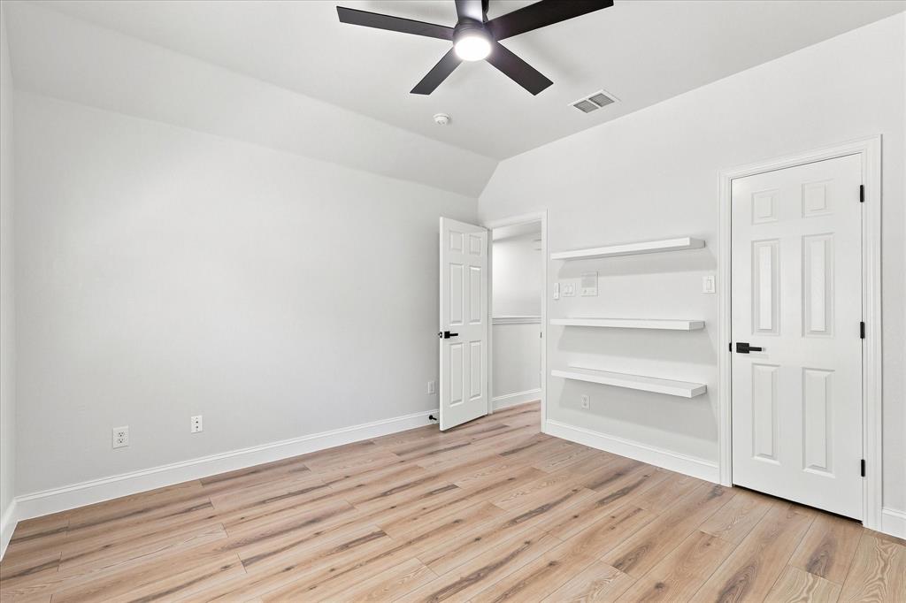 Room featuring wood-finish flooring, three built-in wall shelves, a matte black ceiling fan, and six-panel doors with matte black hardware