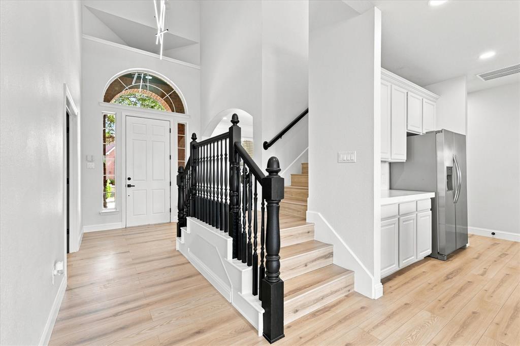 High-ceilinged entry featuring a white arched-top front door with sidelights, wood-finish flooring, and a staircase with black-painted wood balusters and handrails