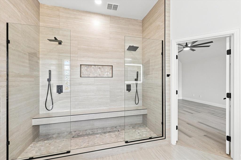 Walk-in shower featuring floor-to-ceiling tile, a built-in stone bench, dual rainfall shower heads with hand-held sprayers, a linear drain, and frameless glass enclosure