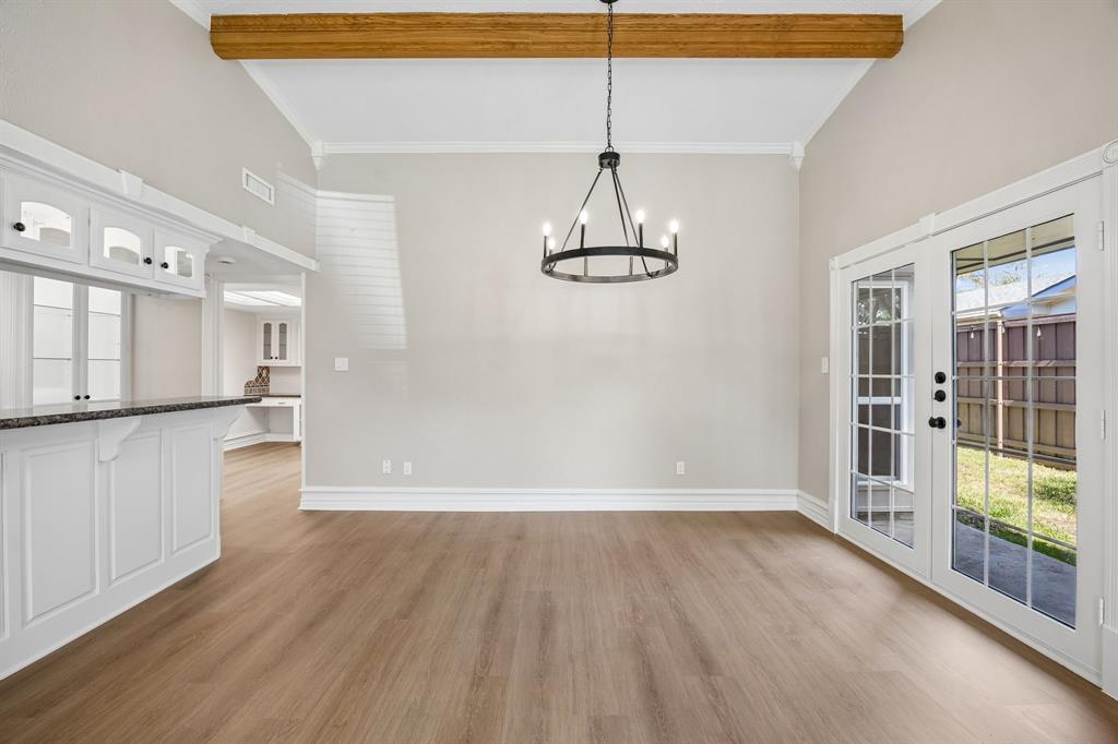 The dining area makes a memorable impression with its decorative exposed wood beam, elegant circular chandelier, and rich wood-look flooring. A built-in serving bar with white cabinetry and dark countertops adds both charm and functionality, while French doors provide a lovely connection to the backyard and allow natural light to flow into the space.
