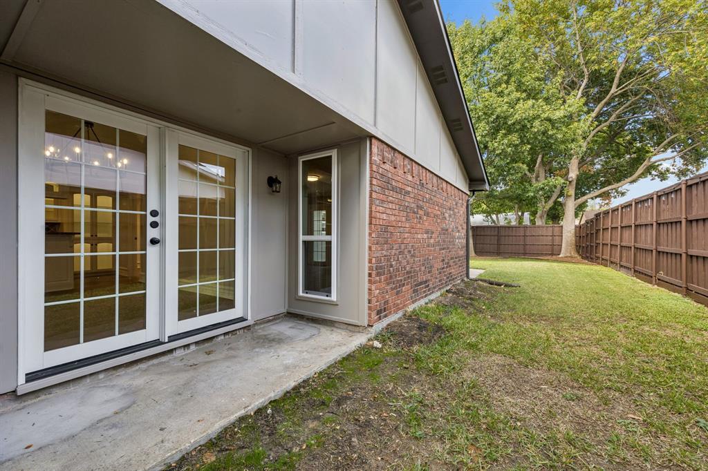 A charming outdoor area combines a concrete patio, classic brick construction, and French doors with a private, fenced backyard. The side yard extends the outdoor space, while mature trees and established greenery contribute natural appeal. Whether enjoying a quiet morning outdoors or hosting casual gatherings, this setting offers a welcoming extension of the home.