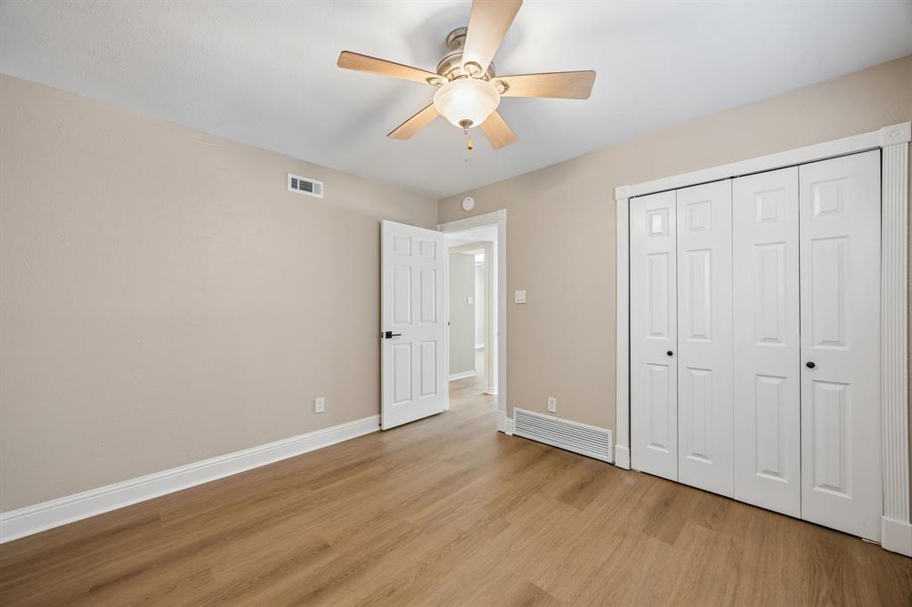 This spacious bedroom features beautiful wood-look flooring, soothing neutral walls, and elegant white trim that creates a clean, cohesive look. A generous double-door closet provides convenient storage, while the ceiling fan and overhead lighting add everyday comfort. The open doorway offers an inviting transition to the adjoining living spaces.