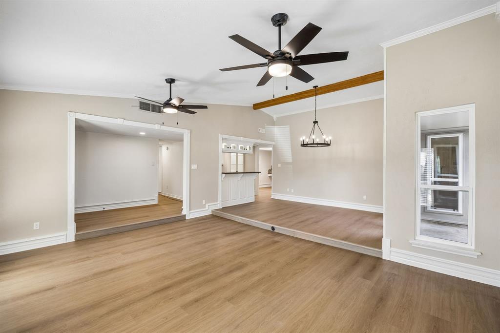 An open, flowing layout connects the spacious living and dining areas, creating an inviting setting for everyday living and entertaining. Beautiful wood-look flooring extends throughout, complemented by soft neutral walls, decorative trim, and ceiling fans. A raised dining area adds architectural definition, while the distinctive exposed wood beam introduces warmth and character.
