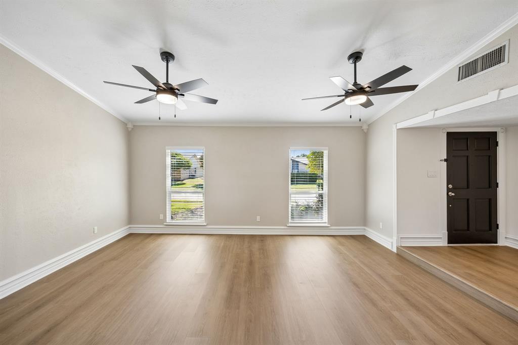 An open, flowing layout connects the spacious living and dining areas, creating an inviting setting for everyday living and entertaining. Beautiful wood-look flooring extends throughout, complemented by soft neutral walls, decorative trim, and ceiling fans. A raised dining area adds architectural definition, while the distinctive exposed wood beam introduces warmth and character.