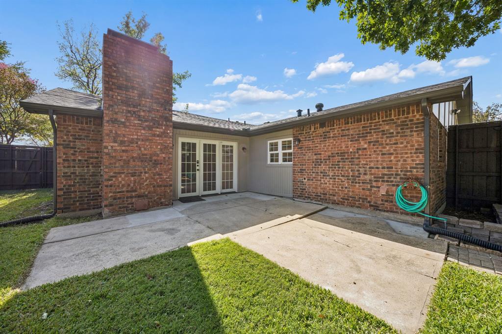 Extend your living space outdoors with this inviting backyard, featuring a spacious concrete patio, classic brick exterior, and charming French doors that connect the interior to the outdoors. The covered section provides a comfortable transition between indoor and outdoor living, while the fenced yard and surrounding greenery offer privacy and room to enjoy the fresh air.