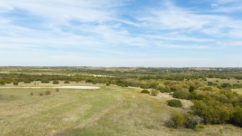 Expansive, undeveloped acreage featuring rolling terrain, native grasses, and clusters of mature trees