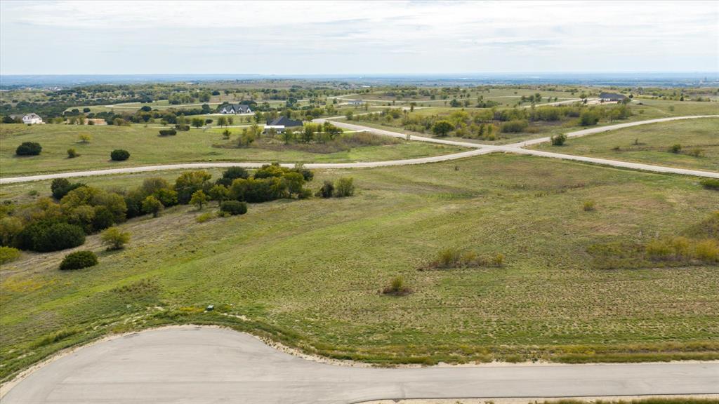Expansive undeveloped land featuring rolling terrain, clusters of mature trees, paved road access, and a panoramic horizon