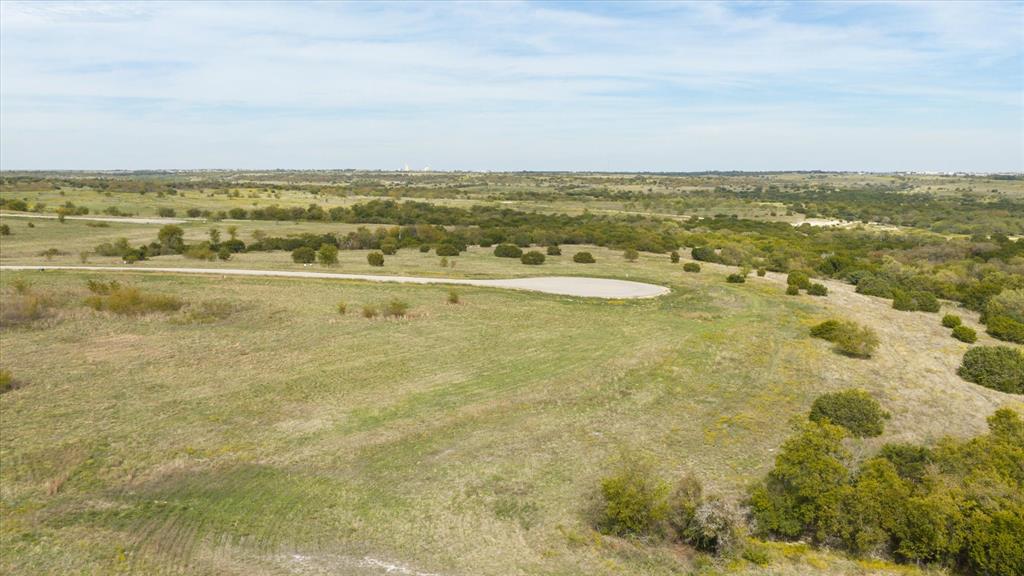 Expansive acreage featuring rolling terrain, native grasses, scattered mature trees, and a paved cul-de-sac