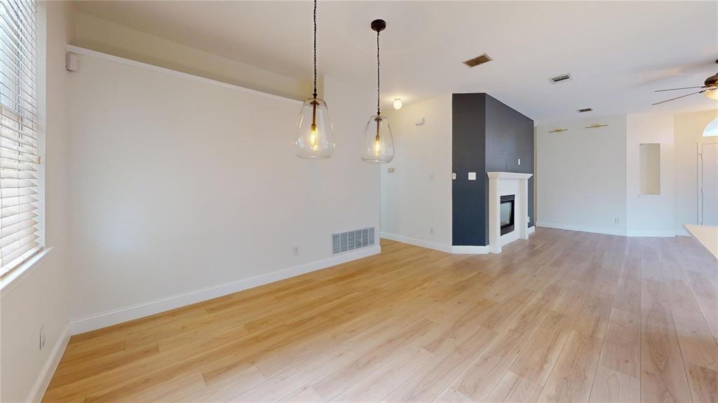 Light-filled interior featuring wood-finish flooring, two glass pendant light fixtures, a fireplace with a decorative mantel, and a neutral color palette