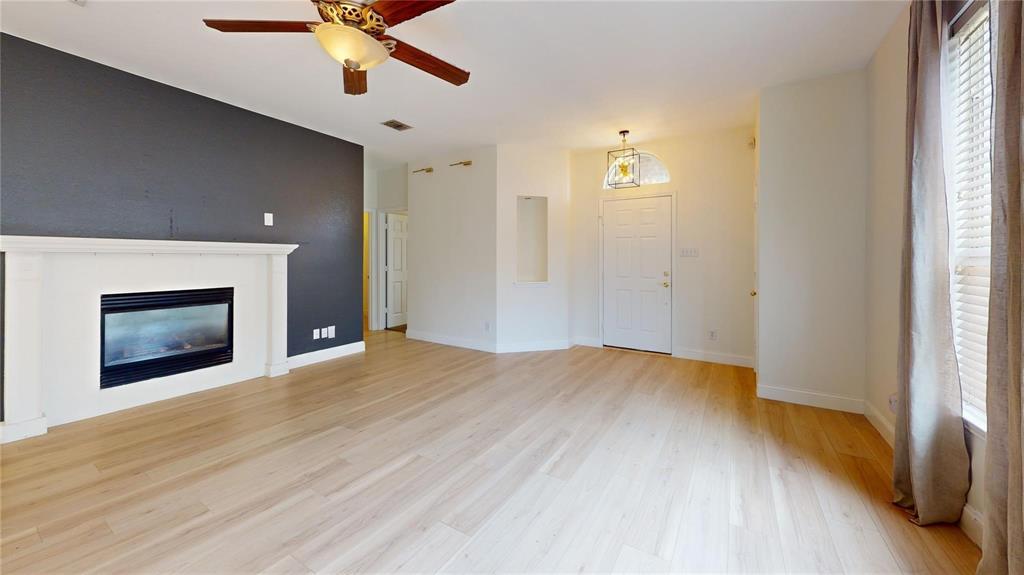 Living area featuring wood-finish flooring, a fireplace with a white mantel, a dark accent wall, recessed wall niche, and a multi-blade ceiling fan