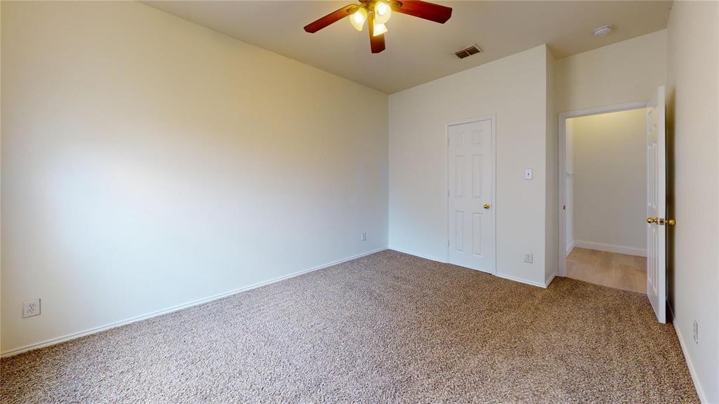 Interior room featuring neutral wall paint, carpeted flooring, a six-panel door, and a ceiling fan with integrated lighting