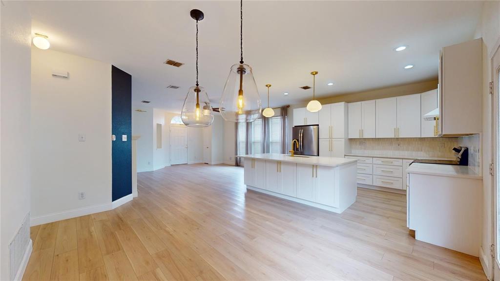 Kitchen featuring white shaker-style cabinetry, central island with stone countertop, wood-finish flooring, gold-tone hardware, and glass pendant lighting