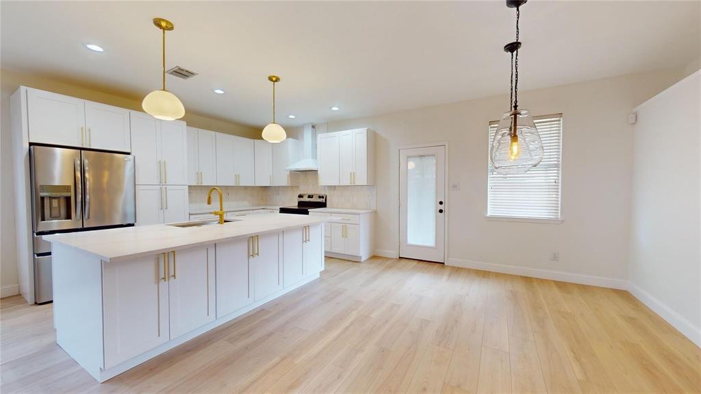 Kitchen featuring white shaker-style cabinetry, quartz countertops, an expansive center island with gold-finish hardware, stainless steel appliances, and wood-finish flooring