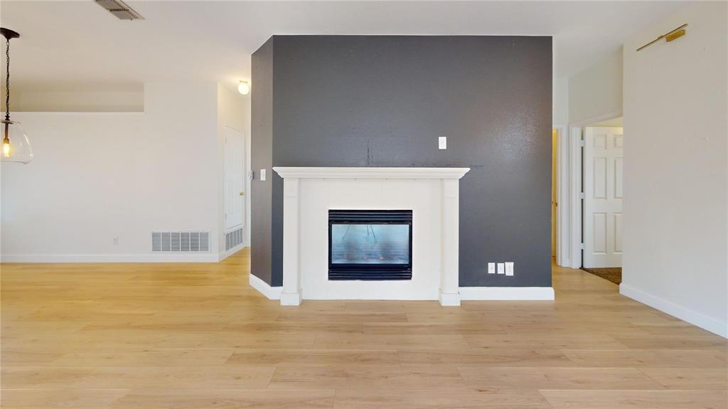 Fireplace with a classic white mantel set against a dark accent wall, featuring wood-finish flooring and a contemporary pendant light fixture