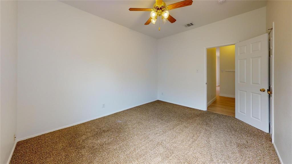 Neutral-toned interior space featuring carpeted flooring, a ceiling fan with integrated lighting, and a six-panel interior door