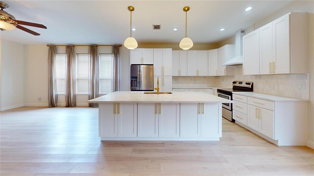 Kitchen featuring white shaker-style cabinetry, quartz countertops, a central island with a built-in sink, gold-tone hardware, and wood-finish flooring