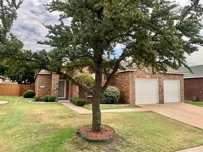 Brick exterior featuring a two-car garage, concrete driveway, and mature landscaping