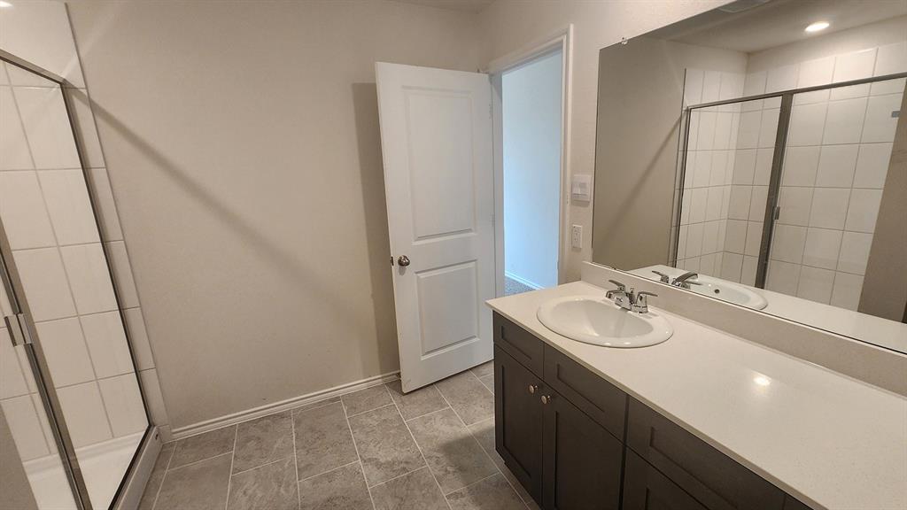 Bathroom featuring a vanity with an integrated sink, polished chrome faucet, expansive mirror, and a tiled shower enclosure