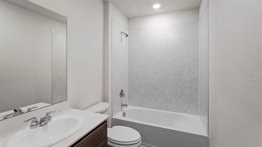 Bathroom featuring a vanity with an integrated basin, a large wall-mounted mirror, a tub-shower combination with patterned wall surround, and chrome fixtures