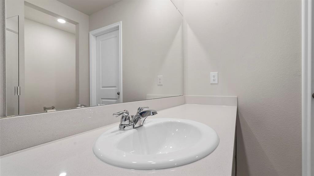 Bathroom vanity featuring a light-toned solid surface countertop, integrated oval sink, polished chrome centerset faucet, and an expansive frameless wall-mounted mirror