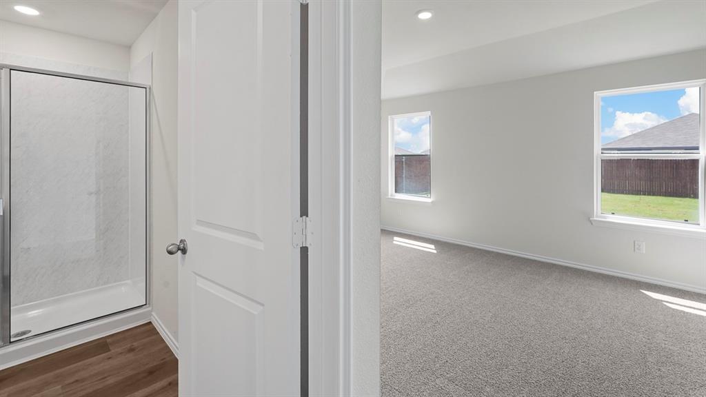 Shower enclosure with integrated surround, wood-finish flooring, neutral carpeting, recessed ceiling lighting, and multiple windows