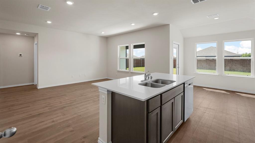 Kitchen island featuring a stone-composite countertop, dual-basin stainless steel sink, wood-finish cabinetry, and recessed lighting throughout the area