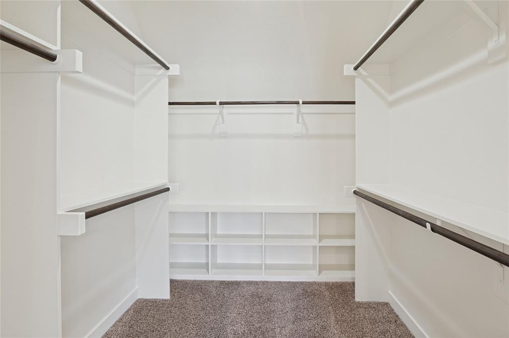 Walk-in storage space featuring built-in white shelving, multiple tiers of garment rods, and wall-to-wall carpeting