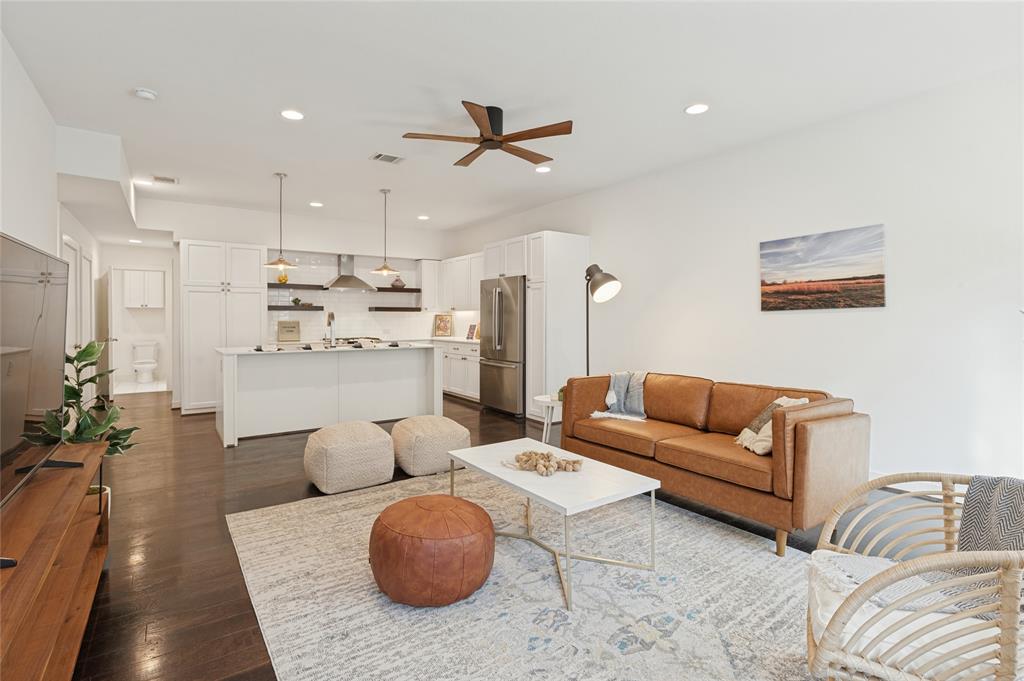 Open-concept kitchen featuring white shaker-style cabinetry, stainless steel appliances, a central island, and wood-finish flooring