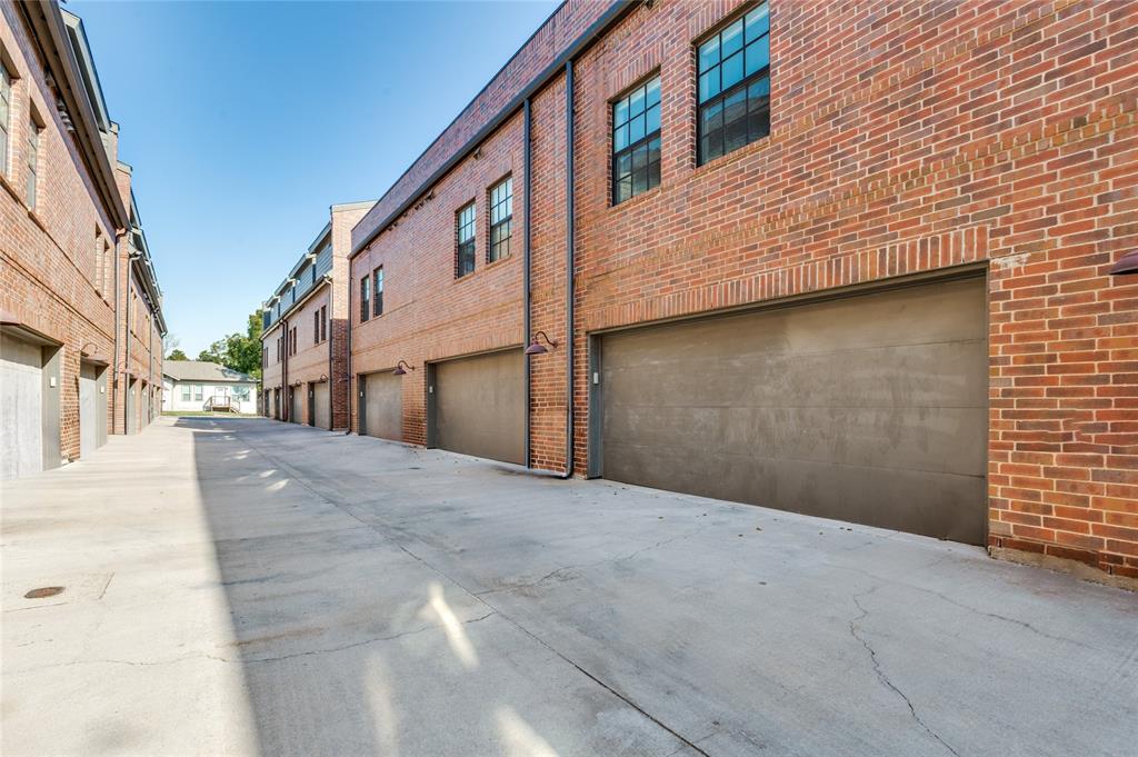 Red brick exterior featuring multi-pane windows, smooth-finish garage doors, and industrial-style gooseneck wall lighting